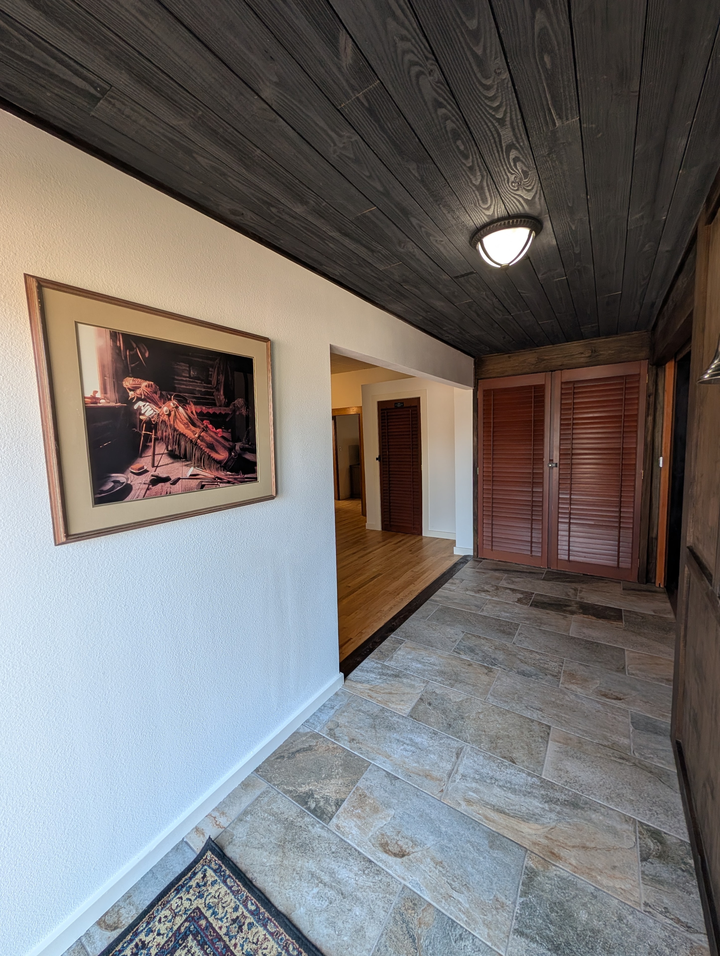 Entryway hallway with dark wood ceiling, tile floors, and framed artwork